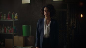 Movie still from “Die Hart” (2023), directed by Eric Appel – A woman standing in a dark room wearing a suit; Medium shot, Over the shoulder angle