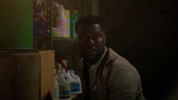 Movie still from “Die Hart” (2023), directed by Eric Appel – A man sitting in front of a shelf of cleaning supplies; Close Up shot, Over the shoulder angle