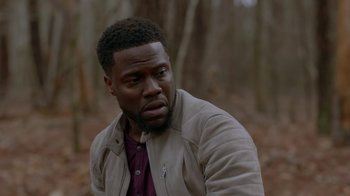 Movie still from “Die Hart” (2023), directed by Eric Appel – A person wearing a jacket near a forest; Close Up shot, Over the shoulder angle