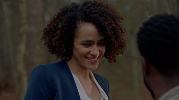 Movie still from “Die Hart” (2023), directed by Eric Appel – A person with curly hair smiling; Close Up shot, Over the shoulder angle