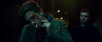 Movie still from “Die in a Gunfight” (2021), directed by Collin Schiffli – A young man with blood all over his face smoking a cigarette; Close Up shot, Over the shoulder angle
