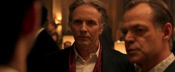 Movie still from “Die in a Gunfight” (2021), directed by Collin Schiffli – A person wearing a suit and tie; Close Up shot, Over the shoulder angle