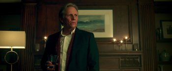 Movie still from “Die in a Gunfight” (2021), directed by Collin Schiffli – A man standing in a room holding a wine glass; Medium shot, Low angle