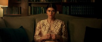 Movie still from “Die in a Gunfight” (2021), directed by Collin Schiffli – A woman sitting in a chair in front of a book shelf; Medium shot, High angle