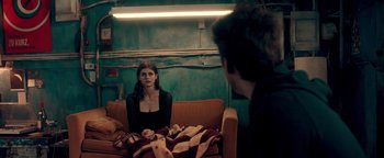 Movie still from “Die in a Gunfight” (2021), directed by Collin Schiffli – A man and a woman sitting on a couch in a room; Medium shot, Over the shoulder angle