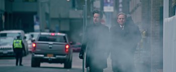 Movie still from “Die in a Gunfight” (2021), directed by Collin Schiffli – Two men walking down the street in the fog; Medium shot, Low angle