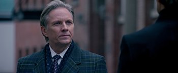 Movie still from “Die in a Gunfight” (2021), directed by Collin Schiffli – An older man in a suit and tie looking to his left; Close Up shot, Over the shoulder angle