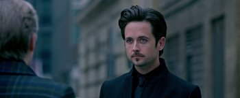 Movie still from “Die in a Gunfight” (2021), directed by Collin Schiffli – A person wearing a suit and tie; Close Up shot, Over the shoulder angle