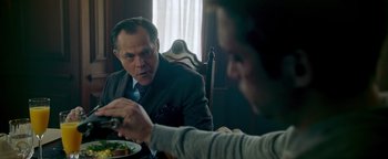 Movie still from “Die in a Gunfight” (2021), directed by Collin Schiffli – A man sitting at a table with a plate of food; Close Up shot, Over the shoulder angle