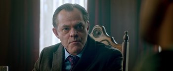 Movie still from “Die in a Gunfight” (2021), directed by Collin Schiffli – A man in a suit and tie sitting in a chair; Close Up shot, Low angle