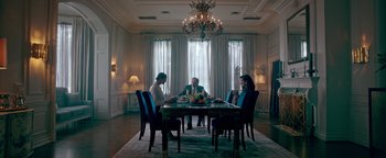 Movie still from “Die in a Gunfight” (2021), directed by Collin Schiffli – A group of people sitting at a table in front of a window; Wide shot, Low angle