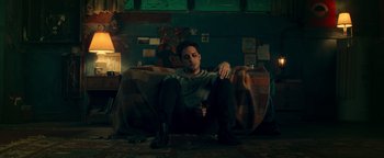 Movie still from “Die in a Gunfight” (2021), directed by Collin Schiffli – A man sitting on top of a couch in a room; Medium shot, High angle