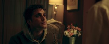 Movie still from “Die in a Gunfight” (2021), directed by Collin Schiffli – A man sitting in front of a lamp in a room; Close Up shot, Over the shoulder angle