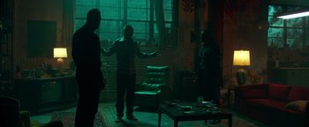 Movie still from “Die in a Gunfight” (2021), directed by Collin Schiffli – A group of people standing in a living room; Wide shot, High angle