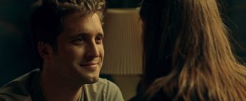 Movie still from “Die in a Gunfight” (2021), directed by Collin Schiffli – A man sitting next to a woman in front of a lamp; Close Up shot, Over the shoulder angle