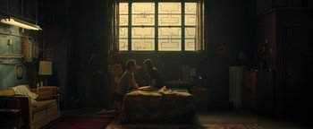 Movie still from “Die in a Gunfight” (2021), directed by Collin Schiffli – Two people sitting on a bed in front of a large window; Wide shot, High angle