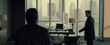 Movie still from “Die in a Gunfight” (2021), directed by Collin Schiffli – A person sitting at a desk in front of a window; Wide shot, Over the shoulder angle