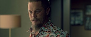 Movie still from “Die in a Gunfight” (2021), directed by Collin Schiffli – A person with a beard wearing a floral shirt; Close Up shot, Over the shoulder angle
