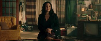 Movie still from “Die in a Gunfight” (2021), directed by Collin Schiffli – A woman sitting on a chair in front of a window; Medium shot, Over the shoulder angle