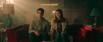 Movie still from “Die in a Gunfight” (2021), directed by Collin Schiffli – A man and a woman sitting on a red couch; Medium shot, Low angle