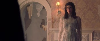 Movie still from “Die in a Gunfight” (2021), directed by Collin Schiffli – A woman standing in front of a mirror in a room; Medium shot, Low angle