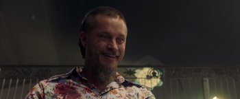 Movie still from “Die in a Gunfight” (2021), directed by Collin Schiffli – A man with a beard wearing a floral shirt; Close Up shot, Over the shoulder angle