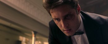 Movie still from “Die in a Gunfight” (2021), directed by Collin Schiffli – A person wearing a suit and tie; Close Up shot, Low angle
