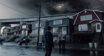 Movie still from “War of the Worlds” (2005), directed by Steven Spielberg – A man standing in the rain in front of a building; Extreme Wide shot, Low angle