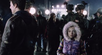 Movie still from “War of the Worlds” (2005), directed by Steven Spielberg – A little girl wearing a purple jacket standing in front of a group of people; Medium shot, Over the shoulder angle