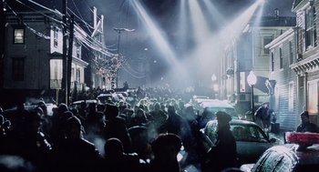 Movie still from “War of the Worlds” (2005), directed by Steven Spielberg – A group of people sitting on the sidewalk at night; Extreme Wide shot, High angle