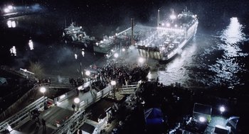 Movie still from “War of the Worlds” (2005), directed by Steven Spielberg – A group of people standing next to a body of water at night; Extreme Wide shot, High angle