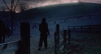 Movie still from “War of the Worlds” (2005), directed by Steven Spielberg – A person standing on a dirt road near a field; Wide shot, Over the shoulder angle