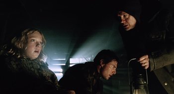 Movie still from “War of the Worlds” (2005), directed by Steven Spielberg – A group of people in a dark room with lights on; Medium shot, Over the shoulder angle