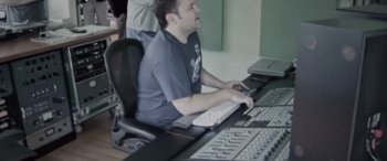 Movie still from “Dio: Dreamers Never Die” (2022), directed by Demian Fenton – A man sitting in front of a computer keyboard; Medium shot, High angle
