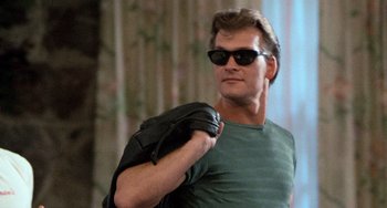 Movie still from “Dirty Dancing” (1987), directed by Emile Ardolino – A man wearing sunglasses and holding a black bag; Close Up shot, Low angle