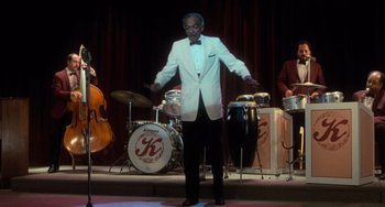 Movie still from “Dirty Dancing” (1987), directed by Emile Ardolino – A man in a white suit and bow tie on stage; Wide shot, Low angle