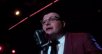 Movie still from “Dirty Dancing” (1987), directed by Emile Ardolino – A man in a suit and tie holding a microphone; Close Up shot, Low angle