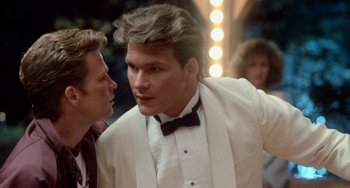 Movie still from “Dirty Dancing” (1987), directed by Emile Ardolino – Two men in tuxedos talking to each other in front of a crowd; Close Up shot, Over the shoulder angle