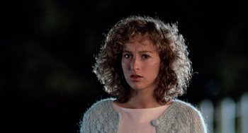 Movie still from “Dirty Dancing” (1987), directed by Emile Ardolino – A woman with curly hair is standing in the dark; Close Up shot, Over the shoulder angle