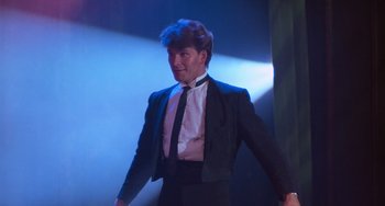 Movie still from “Dirty Dancing” (1987), directed by Emile Ardolino – A man wearing a suit and tie standing in front of lights; Medium shot, Low angle