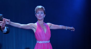 Movie still from “Dirty Dancing” (1987), directed by Emile Ardolino – A woman in a pink dress with her arms outstreched; Medium shot, Low angle