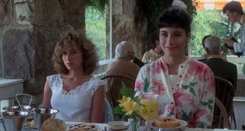 Movie still from “Dirty Dancing” (1987), directed by Emile Ardolino – Two women are sitting at a table with food and drinks; Medium shot, Over the shoulder angle