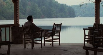 Movie still from “Dirty Dancing” (1987), directed by Emile Ardolino – A man sitting at a table on a deck overlooking a body of water; Wide shot, High angle