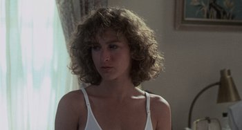 Movie still from “Dirty Dancing” (1987), directed by Emile Ardolino – A young woman with curly brown hair wearing a white tank top; Close Up shot, Over the shoulder angle