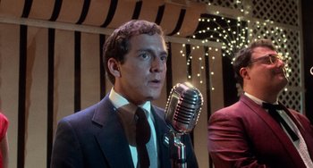 Movie still from “Dirty Dancing” (1987), directed by Emile Ardolino – A man wearing a suit and tie holding a microphone; Close Up shot, Low angle