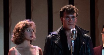 Movie still from “Dirty Dancing” (1987), directed by Emile Ardolino – A man and a woman standing next to each other in front of a microphone; Medium shot, Low angle