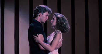 Movie still from “Dirty Dancing” (1987), directed by Emile Ardolino – A man and a woman are holding each other in front of a wall; Medium shot, Low angle