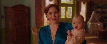 Movie still from “Disenchanted” (2022), directed by Adam Shankman – A woman holding a baby in her arms and smiling for the camera; Close Up shot, Over the shoulder angle