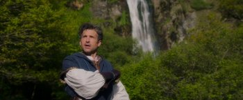 Movie still from “Disenchanted” (2022), directed by Adam Shankman – A man standing in front of a large waterfall; Medium shot, Over the shoulder angle