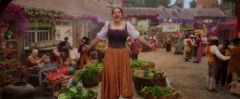Movie still from “Disenchanted” (2022), directed by Adam Shankman – A woman in an orange and black dress standing in a market; Wide shot, Low angle